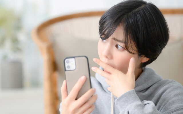 スマホを持ち考える女性
