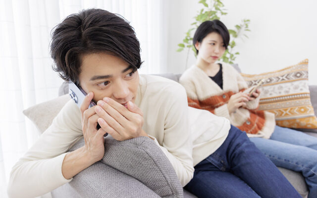 妻に隠れながらスマートフォンで話す夫