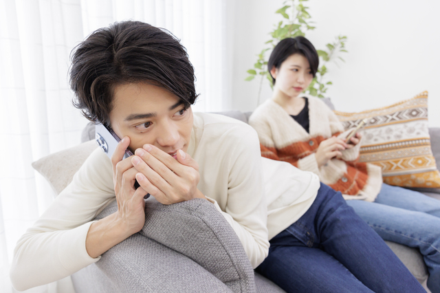 妻に隠れながらスマートフォンで話す夫