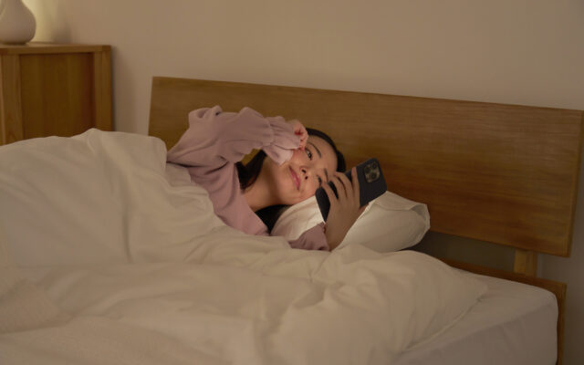 布団の中でスマホを使う女性　眠気