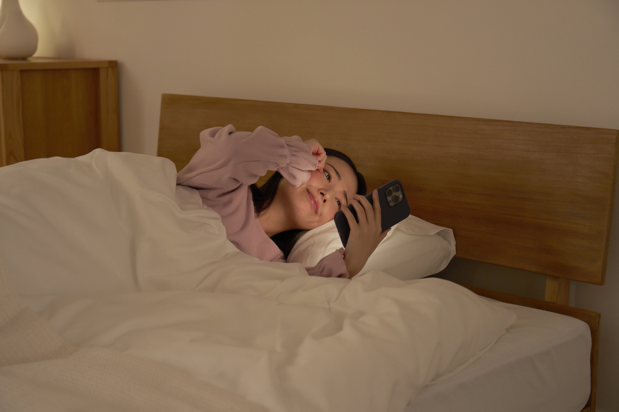 布団の中でスマホを使う女性　眠気